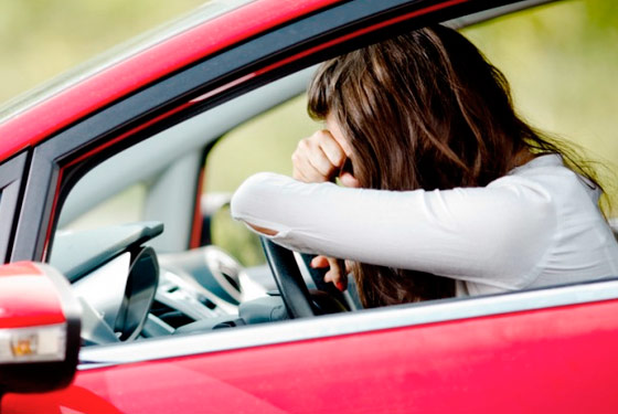 Enquadramento da janela de um carro vermelho com uma mulher debruçada sobre o volante do veículo. A imagem é ilustrativa não corresponde a realidade do fato noticiado