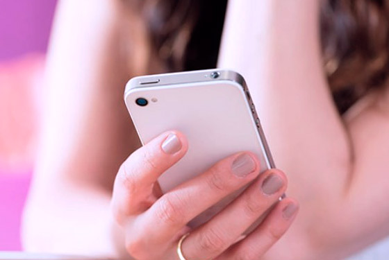 Fotografia do tronco de uma mulher com a mão em primeiro plano segurando um celular