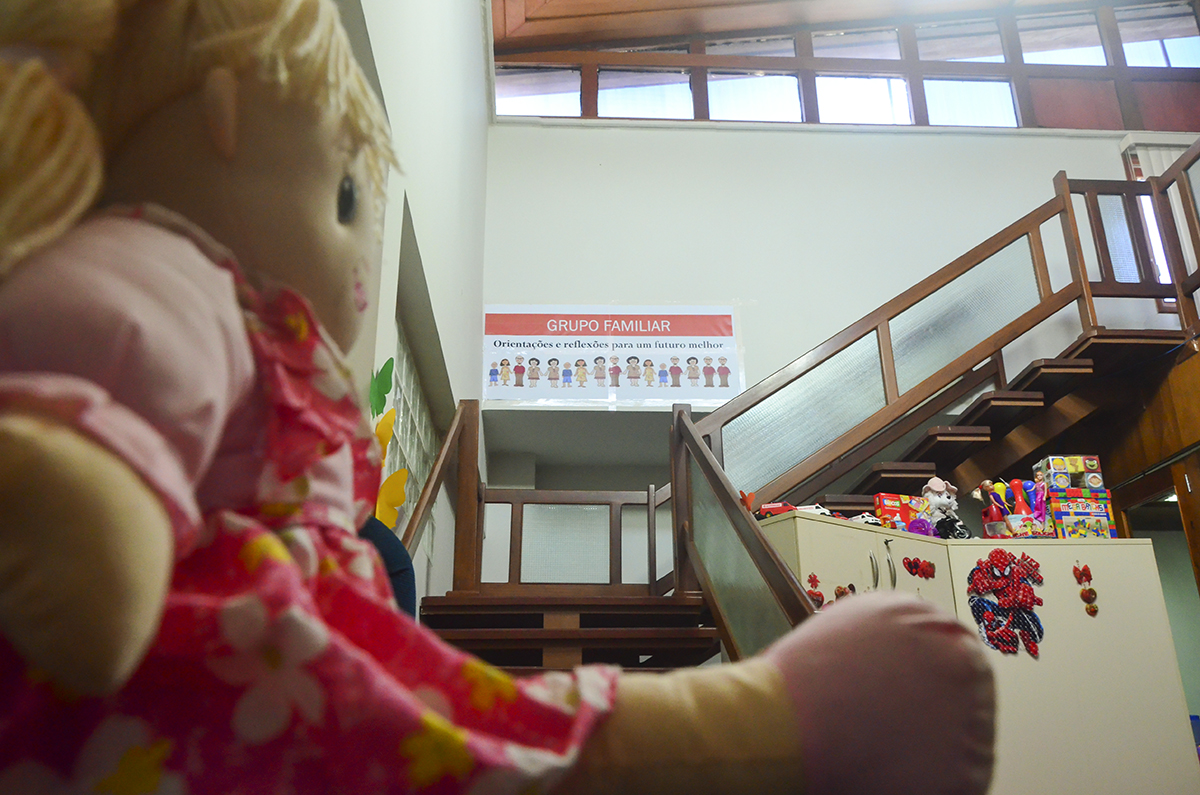 Fotografia de uma boneca sentada no início de uma escada e na parede da escada o cartaz com o nome do Grupo de Orientação familiar