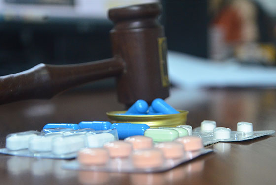 Foto do martelo de juiz ao fundo sob uma mesa marrom e na frente cartelas de remédios nas cores rosa, branco e azul