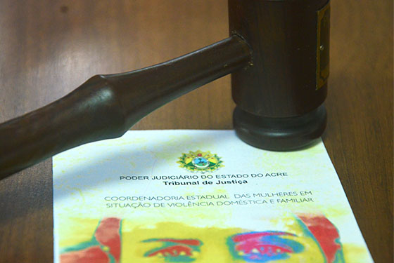 Foto do martelo de juiz sobre um folder da Coordenadoria Estadual das Mulheres em Situação de Violência Doméstica e Familiar
