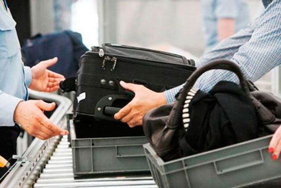 fotografia de esteira de bagagem com duas malas e duas pessoas, uma de cada lado.