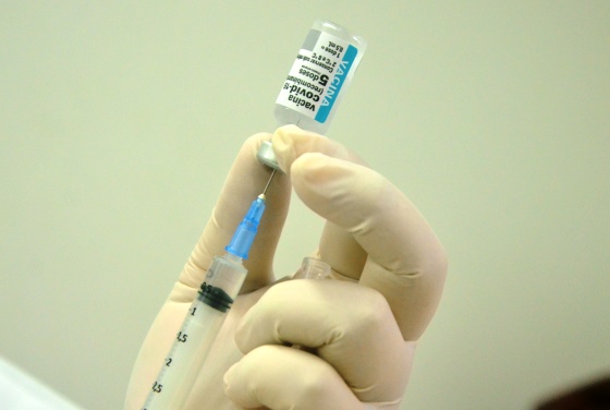 Imagem de uma mão segurando um vidrinho de dose da vacina com uma seringa extraindo o líquido