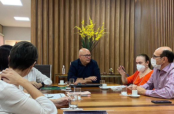 Fotografia de seis pessoas sentada em uma mesa de reunião conversando.