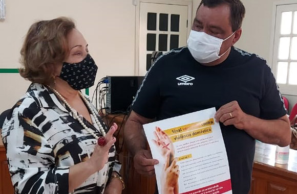 Desembargadora Eva Evangelista conversando com prefeito da cidade, que está segurando um cartaz da Campanha Sinal Vermelho contra a Violência Doméstica