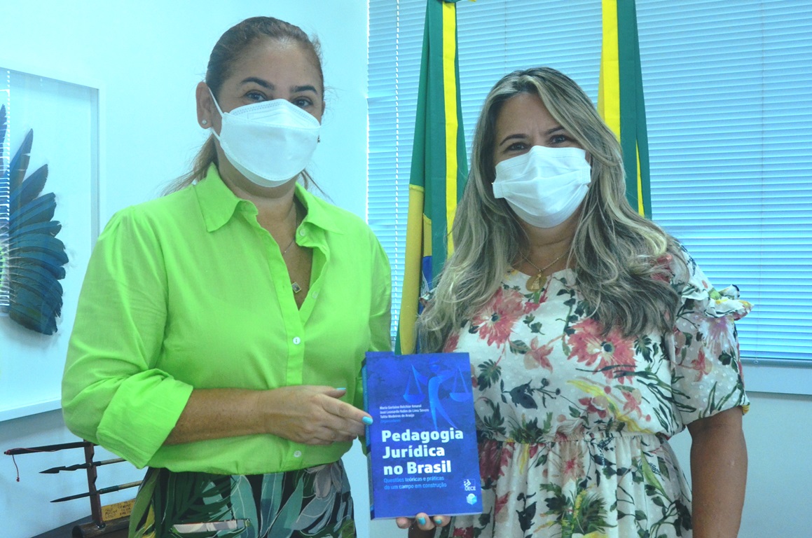 Imagem da presidente, desembargadora Waldirene Cordeiro segurando o livro ao lado da servidora Alessandra Gonçalves. Ambas estão de pé.
