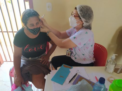 Psicologa atendendo uma mulher. A profissional está mexendo na orelha da moradora