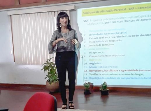 fotografia da psicologa Cláudia de pé falando, ao seu lado uma tela de projeção com slides sobre alienação parental