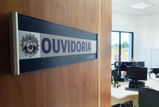 Imagem da porta da Ouvidoria entreaberta com destaque para placa na porta, onde está escrito "Ouvidoria"