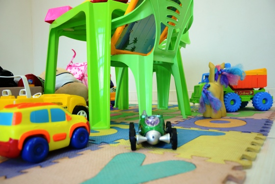 Imagem de uma mesa para criança se sentar na cor verde e no chão um tapete de EVA com letras do alfabeto, assim como, brinquedos esparramados