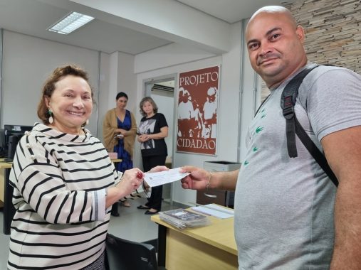 Foto da desembargadora Eva Evangelista entregando título de eleitor para um homem. Ambos olham para foto e sorriem