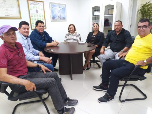 Cinco vereadores e a desembargadora Eva em uma mesa olhando e sorrindo