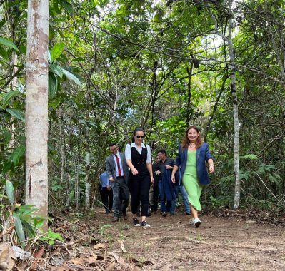 Pessoas andando numa trilha. Presidente sorrindo. Ela usa vestido verde e tênis.