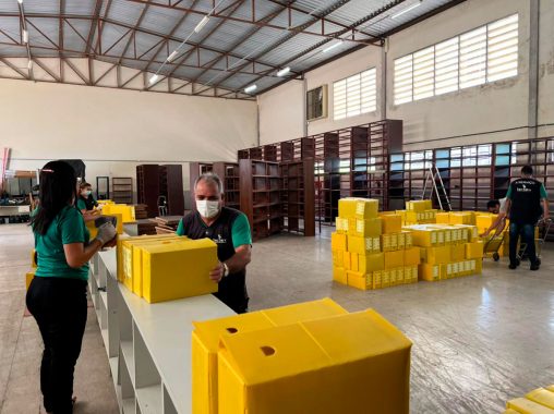 Foto de pessoas do serviço geral colocando caixas amarelas de arquivo em estante