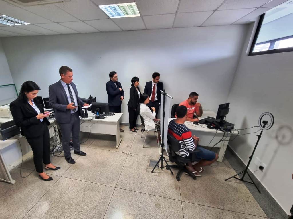Foto da equipe do CNJ observando servidor do Judiciário do Acre fazer a biometria de pessoa que teve a prisão mantida. A pessoa está de costas.