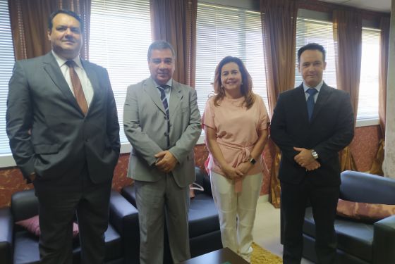 Imagem dos três homens e da desembargadora de pé, olhando para frente e sorrindo. Eles estão dentro de uma sala com cortinas nas janelas e sofás pretos atrás