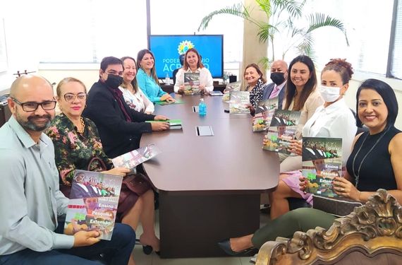 Várias pessoas sentadas em volta de uma mesa grande. Olhando para foto e sorrindo