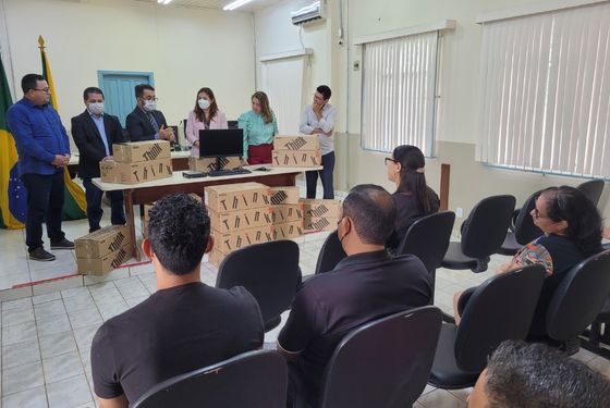 Foto de servidores sentados no plenário do Tribunal do Júri e membros da gestão de pé atrás das caixas com os novos computadores