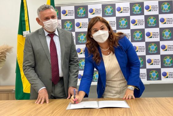 Desembargadora assinando documento. Outro desembargador ao lado