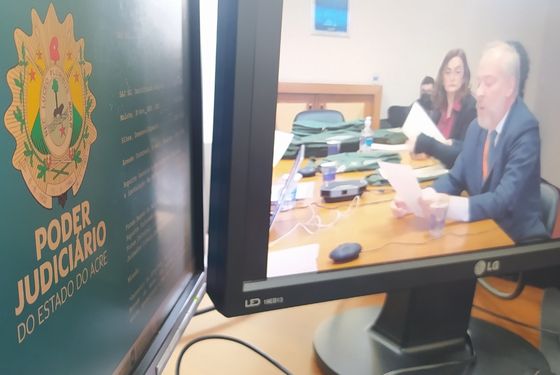imagem de dois monitores de computador, um mostrando a logomarca do TJAC e ou outro a transmissão da sessão de leitura das notas
