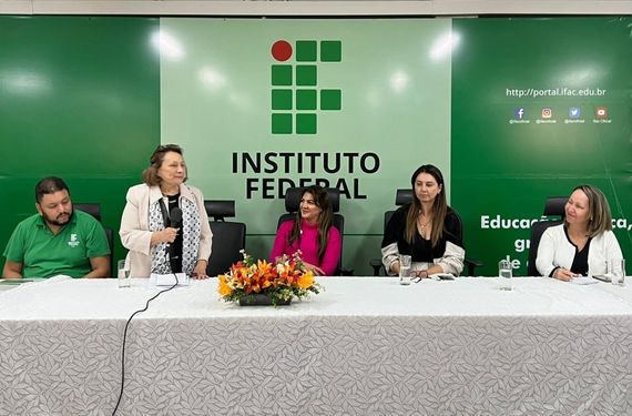 Três mulheres e um homem a frente de um painel verde do IFAC