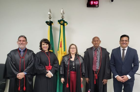 Cinco pessoas em frente as bandeiras do Acre e do Brasil sorrindo para foto