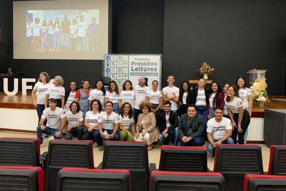 Vinte e cinco pessoas em frente a um palco, sorrindo para foto