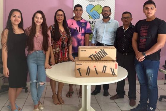 Sete pessoas, sorrindo para foto, a frente de uma mesa com caixas de computadores