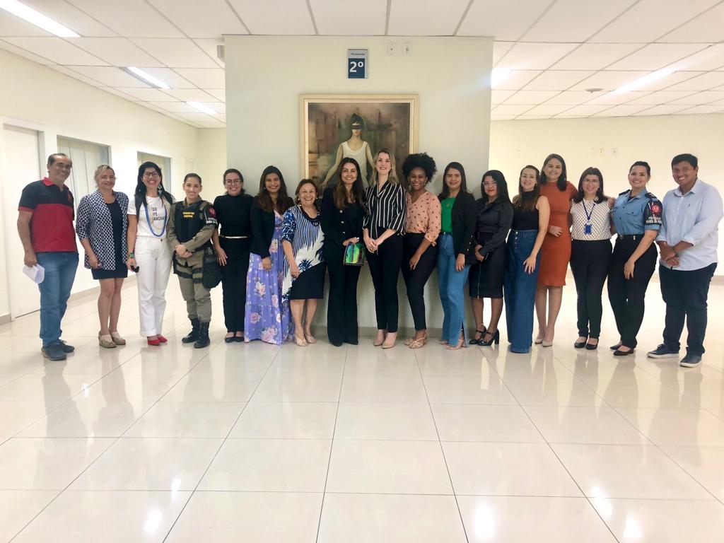 Fotografia com as 17 pessoas que participaram da reunião de preparação da Semana Justiça pela Paz em Casa. Todos estão em pé, lado a lado, frente a um quadro que possui o desenho do símbolo da Justiça