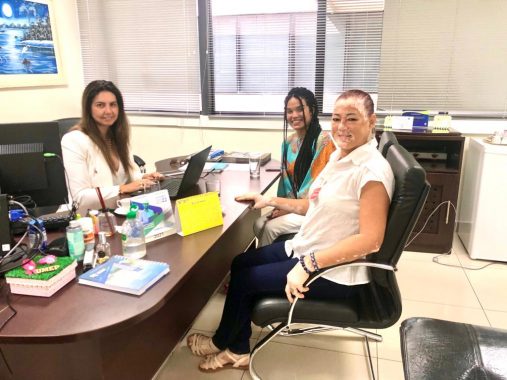 Fotografia da reunião entre a juíza Andrea Brito e a professora Salete Peixoto, acompanhada pela servidora Jenifer. Todas estão sentadas frente a frente no gabinete da juíza e sorrindo para a foto