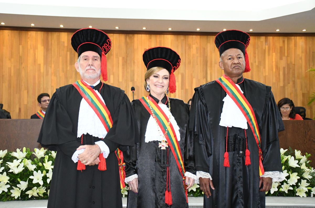 Foto dos três novos gestores do TJ, desembargador Luiz Camolez, Regina Ferrari e Samoel Evangelista. Todos vestem togas preta com detalhes em vermelho e faixa de grão-mestre atravessada na diagonal sobre a roupa. A presidente ainda está com usando o grão-colar.