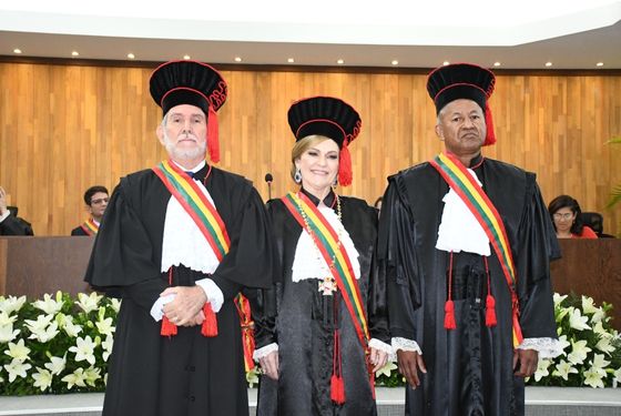 Foto dos três novos gestores do TJ, desembargador Luiz Camolez, Regina Ferrari e Samoel Evangelista. Todos vestem togas preta com detalhes em vermelho e faixa de grão-mestre atravessada na diagonal sobre a roupa. A presidente ainda está com usando o grão-colar.