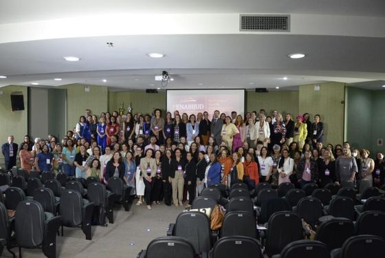 Foto de auditório onde todas as cadeiras estão vazias e os participantes estão de pé dispostos no palco, posando para foto.