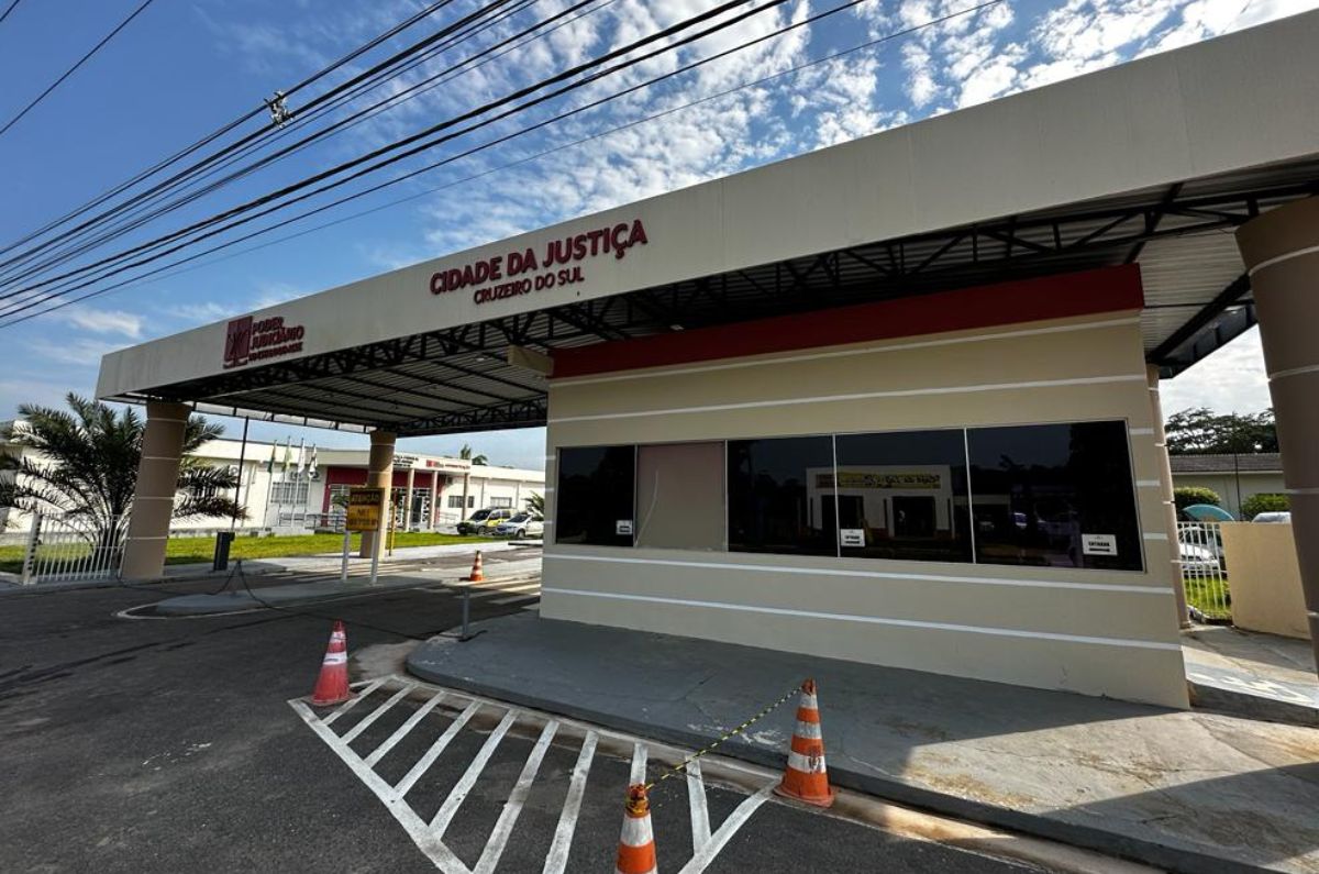 Foto da entrada da Cidade da Justiça de Cruzeiro do Sul. Mostrando a guarita, cones de transito na frente. A guarita é coberta por um grande telhado onde está a logomarca do Poder Judiciário e está escrito "Cidade da Justiça: Cruzeiro do Sul", tudo na cor vermelho escuro
