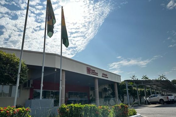Foto da frente do prédio do Fórum Cível e Criminal de Cruzeiro do Sul, mostra-se o local onde estão hasteadas as bandeiras do Brasil e do Acre, um jardim e o estacionamento na lateral do prédio