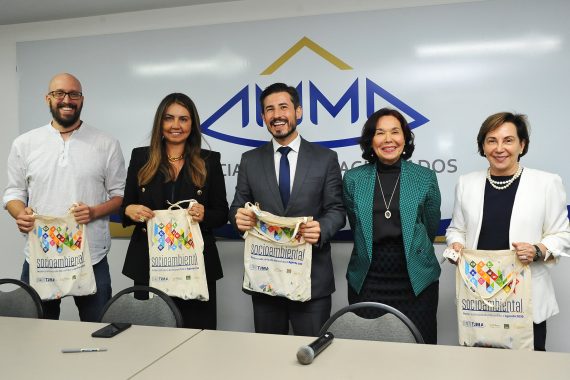 Fotografia dos debatores  apresentando uma sacola de tecido que foi distribuída no evento da Justiça Restaurativa. Há cinco pessoas na foto e a juíza Andrea Brito é a segunda da esquerda para a direita.