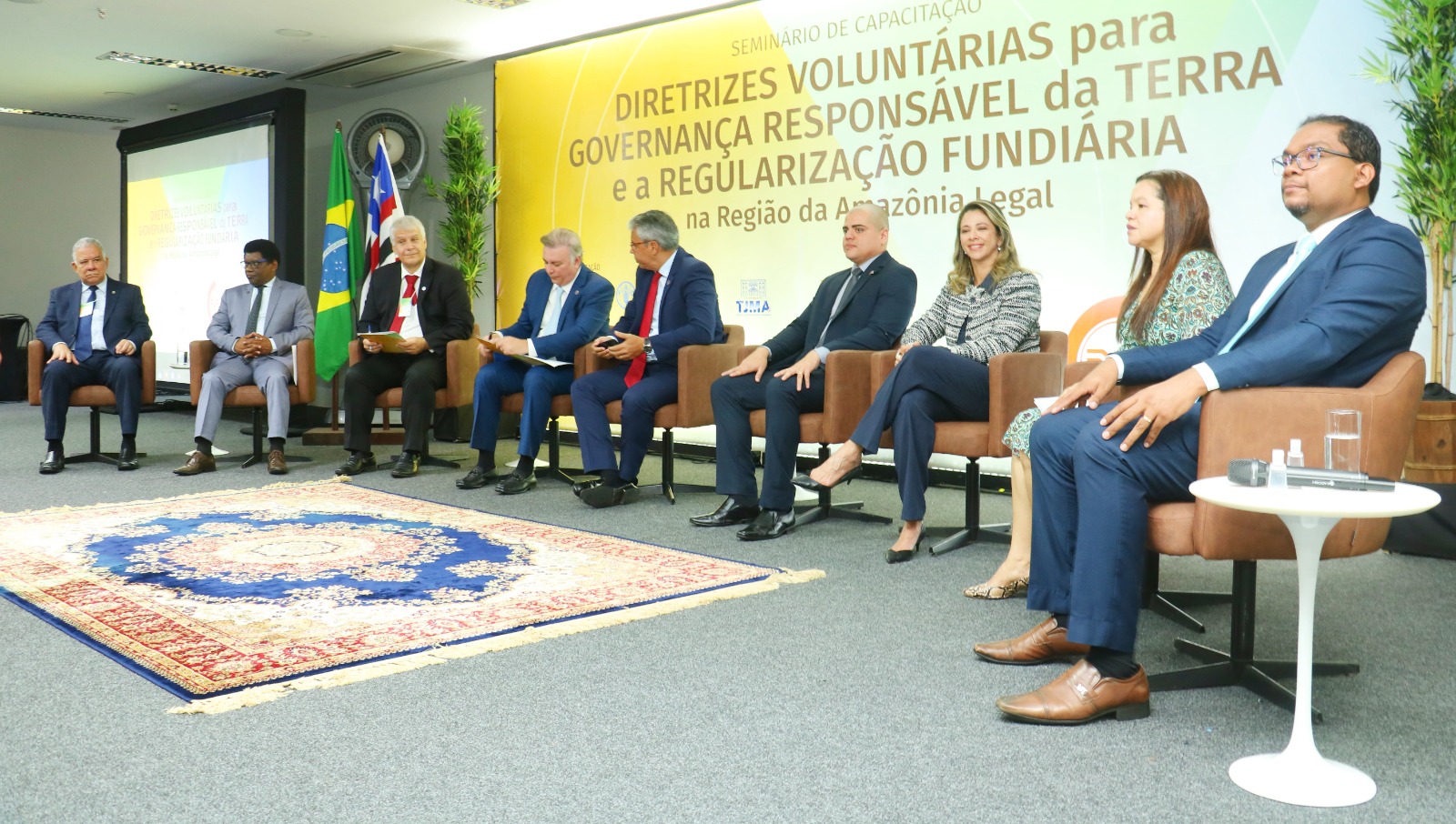 Foto de seis pessoas sentadas e atrás o banner do evento "Seminário Nacional para Governança Responsável da Terra"