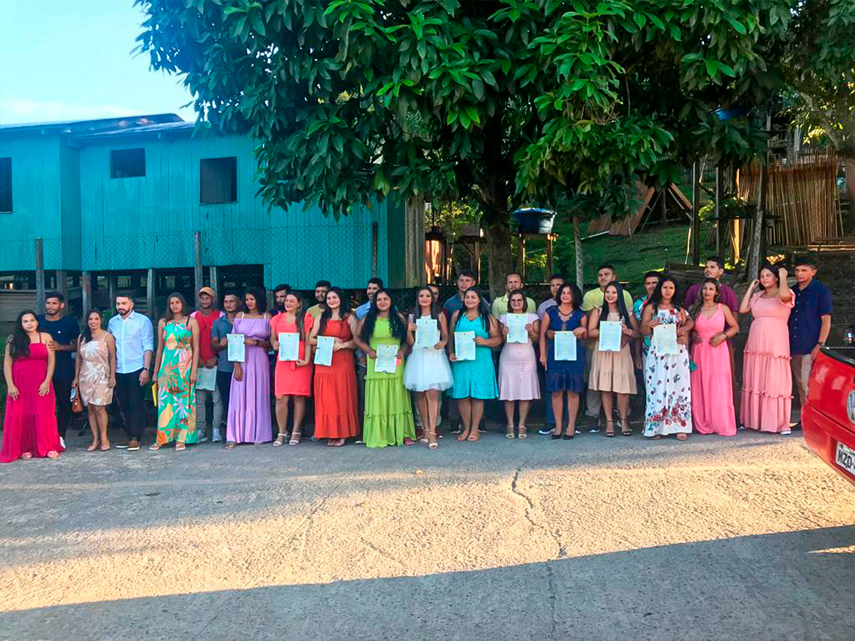 Fotografia dos 10 casais que participaram do casamento coletivo em Marechal Thaumaturgo. Eles estão alinhados na rua com a Certidão de Casamento em mãos