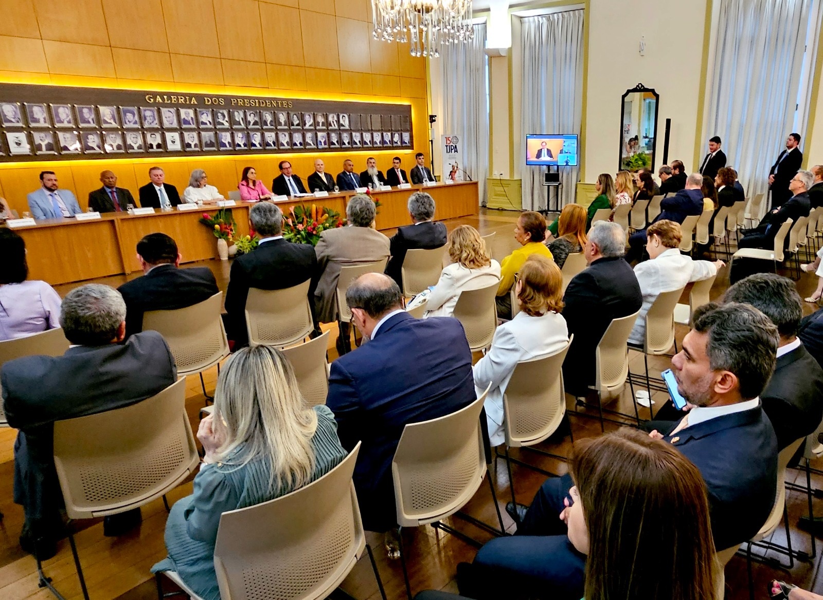 Fotografia da cerimônia de lançamento do Programa Permanente de Regularização Fundiária. O desembargador Samoel Evangelista é a segunda pessoa da esquerda para direita sentado no dispositivo de honra. A frente estão sentados os convidados do evento.