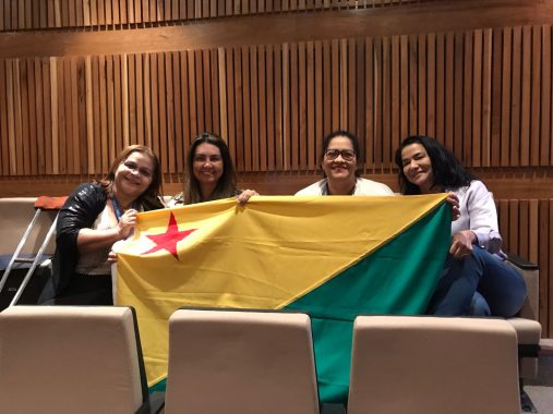 Foto das participantes dos do TJAC e TRE segurando a bandeira do Acre