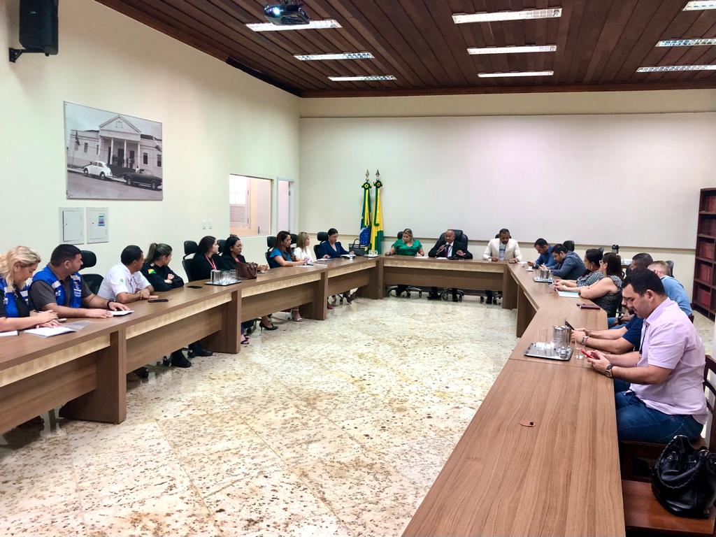 Fotografia da mesa de reunião do Palácio da Justiça, onde estão assentados os representantes das instituições que participarão do evento "Registre-se". Ao centro está o desembargador Samoel Evangelista, corregedor-geral da Justiça, falando ao microfone