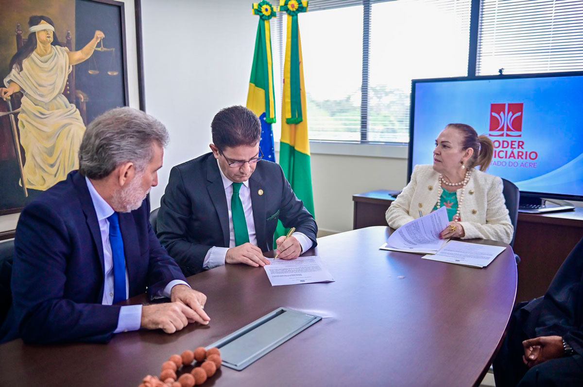 Foto do governador Gladson Cameli assinando documento ao lado da presidente e vice-presidente do TJAC sobre apoio para obras na instituição