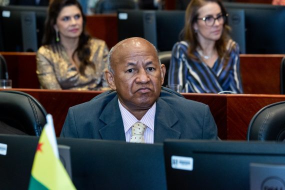 Foto do desembargador Samoel Evangelista sentado na plenária do TJRS e a sua frente há uma pequena bandeira do Acre, simbolizando que ele está representando o TJAC