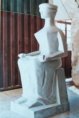 Foto da estátua da deusa Themis pronta no galpão de produção dos artistas. Ela está posicionada de perfil