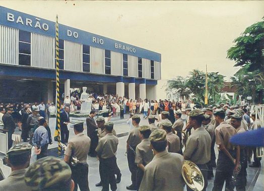 Foto da na reinauguração do Fórum Barão de Rio Branco. O registro foi tirado por trás do público, mostrando então a banda da PM e as pessoas prestigiando a solenidade