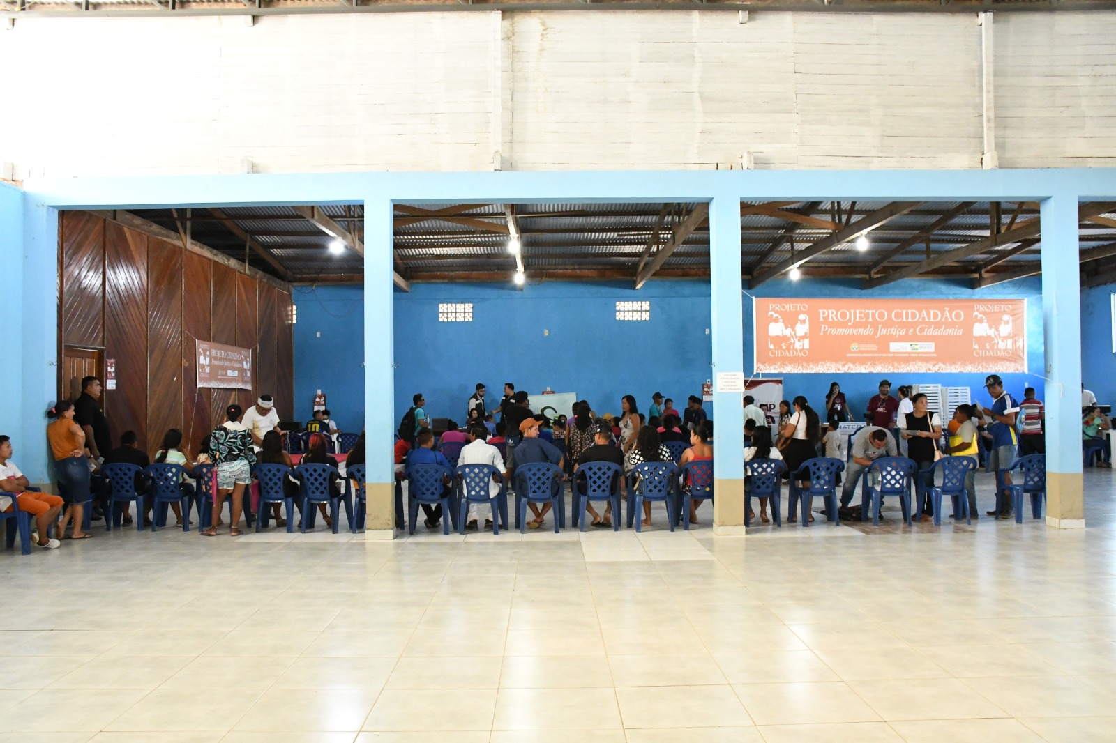 De outro ângulo, foto das pessoas presentes no local, a maioria está sentada esperando o atendimento.