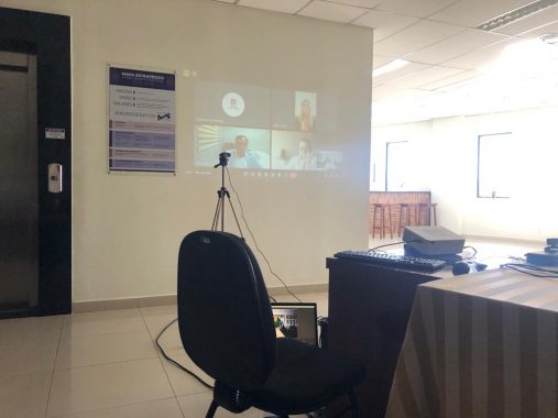 Fotografia da projeção na parede das pessoas da comissão que estão participando por videoconferência da audiência pública. Há cinco pessoas por videoconferência.