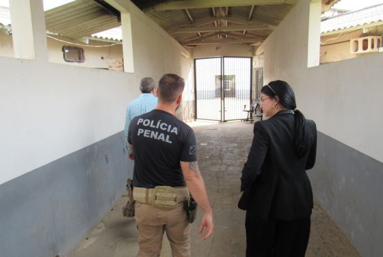 Foto de uma inspeção realizada no presídio. Consta na foto, uma mulher, que aparente ser juíza. Ao seu lado esquerdo, há dois homens, um deles está identificado como polícia penal e o outro de camiseta azul