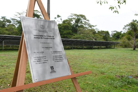 Foto da placa da inauguração da usina fotovoltaica com placas solares ao fundo