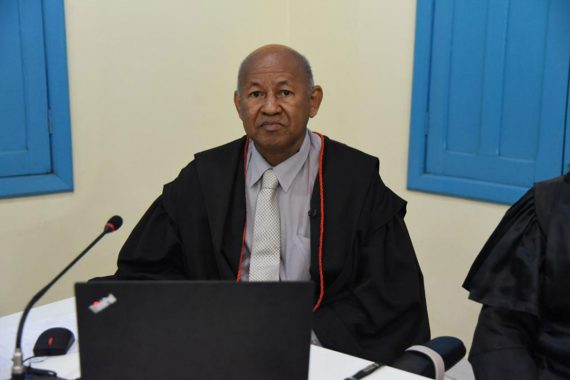 Foto do desembargador Samoel Evangelista. Ele está de toga e camisa lilás. Ele está sentado com um notebook a sua frente. Ele está no Centro Cultural do Juruá.